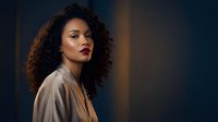 Professional African American businesswoman with curly hair in beige blazer against dark background for corporate branding and marketing materials.