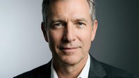 Middle-aged Caucasian male professional wearing dark blazer and open-collar shirt against neutral background. Suitable for corporate, business, leadership, and executive portraits.