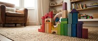 Young child playing with colorful wooden building blocks on living room carpet, creating educational tower structure for early development and learning.