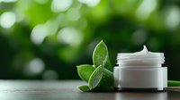 Luxury cosmetic cream jar with fresh green leaves on natural bokeh background, organic skincare and natural beauty product concept.