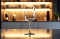 Empty wine glass on reflective surface against warm illuminated bar background with soft bokeh lights creating elegant restaurant atmosphere.