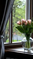 Pink tulips in round glass vase on wooden windowsill with gray curtain and green spring garden view through window, creating cozy home atmosphere.