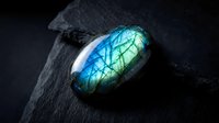 Polished labradorite gemstone with brilliant blue and green flash on dark slate surface for jewelry design and mineral collection displays.