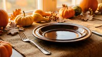 Autumn harvest table setting with empty plate, fork, and spoon surrounded by pumpkins, gourds, and fall leaves on burlap for seasonal dining and holiday entertaining.