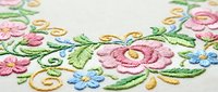 Colorful floral embroidery on cream fabric with pink roses, blue flowers and green leaves in traditional needlework style for textile crafts.