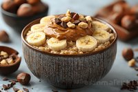 Creamy oatmeal bowl topped with sliced bananas, chocolate spread, hazelnuts and chocolate pieces served in brown ceramic bowl for breakfast or healthy snack.
