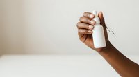Close-up of male hand with medium-dark skin tone holding blank white product packaging against neutral background for branding and marketing mockups.
