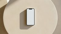 Smartphone with blank white screen on round beige surface, casting shadow, isolated on neutral background, suitable for app mockups and digital design projects.