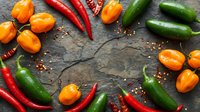 Colorful assortment of fresh hot chili peppers on dark stone background with copy space, including jalapeno, habanero, and cayenne varieties.