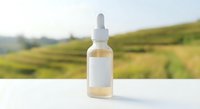 Natural organic serum bottle with dropper on white surface against blurred green landscape background for skincare and wellness product marketing.
