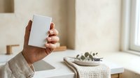 Man with dark skin tone holding blank white mobile phone mockup in modern minimalist interior space with natural lighting for app design and digital product presentation.