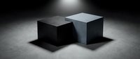 Two contrasting geometric cubes in black and white positioned on concrete surface under dramatic spotlight creating strong shadows and depth.