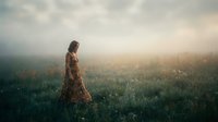 Woman in patterned dress standing in misty meadow at sunrise, surrounded by wildflowers and fog. Suitable for editorial, wellness, and nature-themed designs.