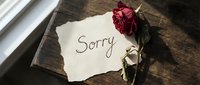 Handwritten sorry note on torn paper with a dried red rose on a rustic wooden surface, evoking apology, regret, and heartfelt emotion.