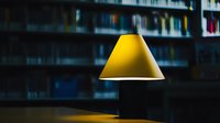 Yellow pendant lamp hanging in dark library interior with blurred bookshelves background creates moody atmospheric lighting scene.