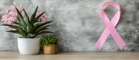 Pink awareness ribbon on gray concrete wall with decorative potted plants and succulents on wooden shelf, breast cancer support symbol and home decor.