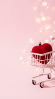 Red heart ornament in miniature shopping cart on pink background with bokeh lights, symbolizing love shopping and Valentine's Day retail sales.