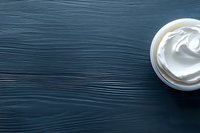 White cosmetic cream in jar on dark blue wooden background with copy space for skincare and beauty product marketing.