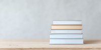 Stack of hardcover books on wooden table against light gray wall background, minimalist composition for education and reading concepts.