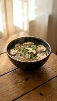 Hot mushroom noodle soup in ceramic bowl on rustic wooden table with warm natural lighting for healthy comfort food and Asian cuisine concepts.
