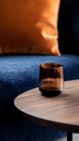 Elegant ribbed amber glass on wooden table against navy blue sofa and copper cushion creates moody atmospheric interior setting with warm lighting effects.