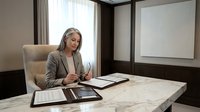 Professional businesswoman working at modern office desk with documents and tablet, corporate executive planning strategy in contemporary workplace.