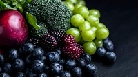 Fresh seasonal berries and fruits on dark background. Healthy organic produce including blueberries, blackberries, grapes, plum and broccoli arranged in rustic style.