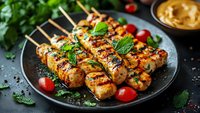 Grilled chicken skewers with fresh herbs and cherry tomatoes on black plate, garnished with mint leaves and served with sauce, close up food photography.