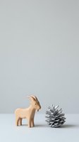 Wooden goat figurine standing beside gray pinecone on white surface against neutral background, isolated for design and decoration use.