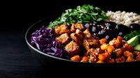Vibrant buddha bowl with roasted sweet potato, black beans, red cabbage, fresh herbs, and quinoa on dark background. Healthy plant-based meal prep concept.