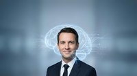 Young adult male professional with dark hair and light complexion wearing formal business attire with glowing brain hologram overlay representing artificial intelligence, innovation, and smart technology solutions.