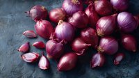 Fresh red onions and peeled cloves scattered on dark textured background, top view of raw organic produce for cooking and food preparation.