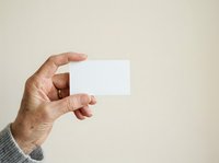 Senior man with weathered skin holding blank white business card or mockup template against neutral beige background, suitable for corporate branding and professional identity design.