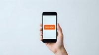 Hand holding smartphone with orange buy now button on screen, showcasing mobile shopping and e-commerce concept on light background.