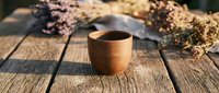 Wooden cup filled with dark beverage on rustic wooden surface surrounded by dried flowers and natural elements, suitable for lifestyle and wellness content.