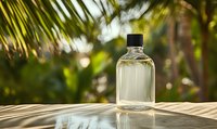 Clear glass bottle with transparent liquid against blurred tropical palm background, creating natural cosmetic or fragrance product atmosphere.