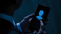 Silhouette of person holding smartphone with glowing social media profile icon in dark blue atmosphere, depicting online identity and digital presence.