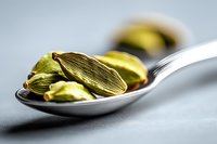 Green cardamom pods on silver spoon against gray background, macro food photography showing aromatic spice detail and texture for culinary and cooking concepts.