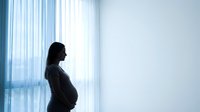 Pregnant woman silhouette standing by window with natural light streaming through curtains in modern interior space for maternity concepts.