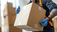 Delivery service worker in protective gloves and uniform carrying cardboard box during contactless delivery. Focus on package and hands for shipping concept.