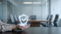 Young professional male hand holding glowing shield with checkmark symbol, representing data security, protection, and trust in modern office conference room setting.