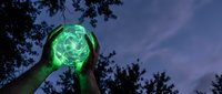 Hands holding glowing green energy orb against twilight sky with tree silhouettes. Mystical power concept for fantasy, magic, supernatural themes and spiritual energy.
