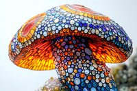 Vibrant mosaic mushroom sculpture featuring intricate dotted patterns in blue, orange, and yellow creates magical garden art atmosphere. Decorative outdoor piece.