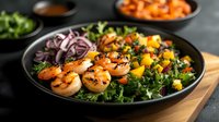 Grilled shrimp kale salad with mango, red onion and butternut squash on black plate. Fresh healthy lunch bowl with colorful vegetables and seafood.