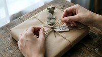 Close-up of hands wrapping kraft paper gift box with twine and eucalyptus branch, thank you tag attached, sustainable packaging and eco-friendly present wrapping concept.
