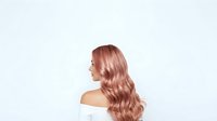 Woman with long wavy rose gold hair styled in loose waves, shown in profile view against white background, suitable for beauty and hair care marketing.