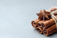 Aromatic cinnamon sticks bundled with twine and star anise on gray background, macro food photography highlighting warm baking spices and natural textures.