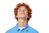 Young redhead male with curly ginger hair looking up with hopeful expression wearing blue polo shirt and white t-shirt on white background, isolated portrait.