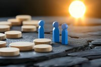 Blue wooden figures standing among scattered pills on dark surface with dramatic sunset lighting, representing healthcare challenges and medical treatment decisions.