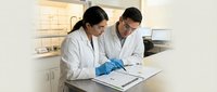 Two professional scientists in white lab coats collaborating over research documents in modern laboratory setting for medical and scientific studies.